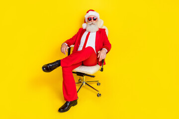 Fototapeta na wymiar Photo of attractive charming retired guy wear red tux claus hat sitting leather chair isolated yellow color background