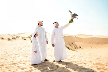 Foto auf Glas Three generation family making a safari in the desert of Dubai. Grandfather, son and grandson spending time together in the nature and training their falcon bird. © oneinchpunch