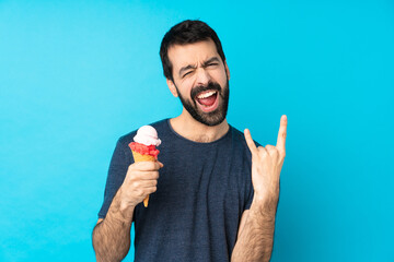 Young man with a cornet ice cream over isolated blue background making rock gesture