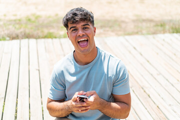 Fototapeta premium Young hispanic man at outdoors surprised and sending a message