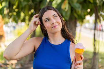 Young pretty Brazilian woman with a cornet ice cream at outdoors having doubts and with confuse...