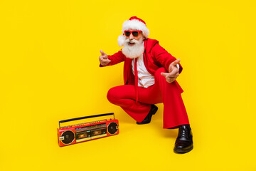 Full length photo of positive cheerful retired guy wear red tux claus hat enjoying boom box music isolated yellow color background © deagreez