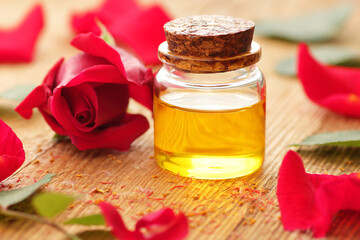Rose essential oil or water in glass bottle with red flowers and petals on textured table, closeup,...