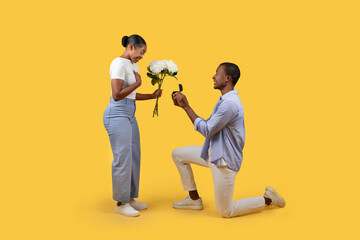 Black man proposing with ring to woman holding flowers