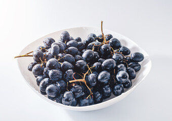 Bunches of blue grapes in white plate on white background. Berries, summer harvest, healthy eating
