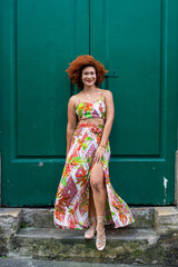 Beautiful redhead woman in long colorful dress standing against a large green colored door.