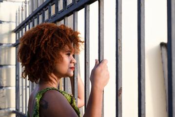 Portrait of the face of a beautiful woman with red hair looking at the sun through an iron railing.
