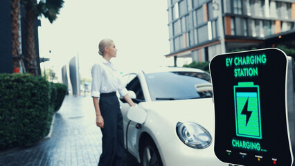 Businesswoman recharge her electric car from charging station at city center or public parking car....