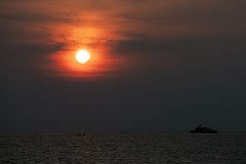 Scenic golden red sunset, Sun partly behind clouds, Tropical sky, silhouettes of military ship and small fishing boats at horizon line