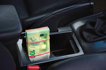 Stack of EUR banknotes in the niche of central console of car. Money pack. Euro money banknotes. Bundle of 100 euro bills. Selective focus.