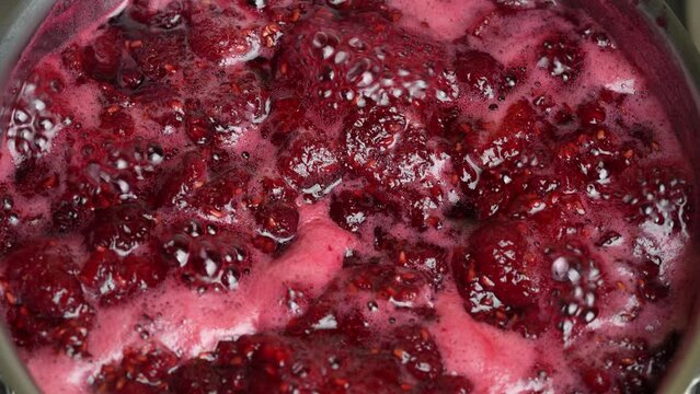 Preparation of freshly picked red raspberries with sugar to make raspberry jam, close up. Cooking homemade raspberry fruit jam in a saucepan. Boiling raspberry fruits for jam