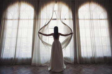 Bride near the window. the bride in a wedding dress opens the curtains of the window, stands back,...