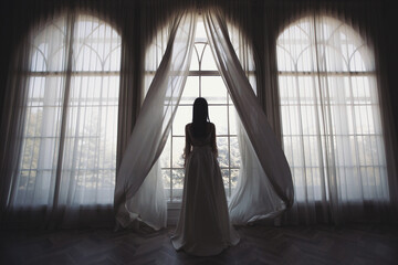 Bride near the window. the bride in a wedding dress opens the curtains of the window, stands back,...