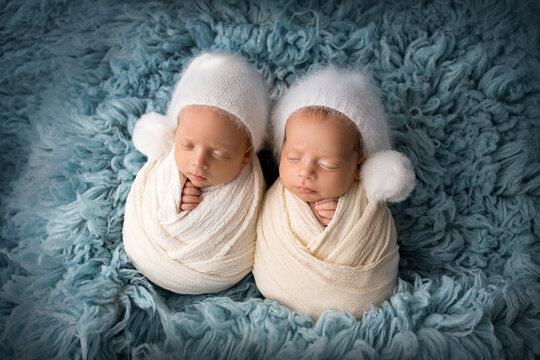 Tiny newborn twin boys in white cocoons on a blue background in white caps. Studio professional photography of newborn baby twins. Twin brothers.