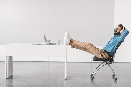 Relaxed indian man with feet up at office desk, side view