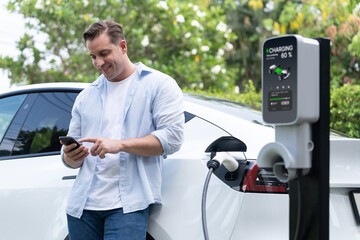 Modern eco-friendly man recharging electric vehicle from EV charging station, using Innovative EV...