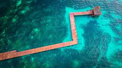 Wooden boardwalk without railing in tropical ocean with sandy coral below clear tropical water