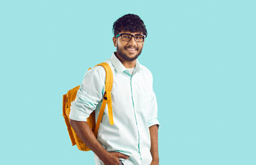 Studio shot of ethnic male student. Portrait of college or university student with backpack. Happy young Indian man in white shirt and glasses standing on light blue background