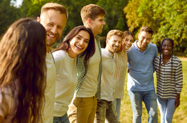 Happy diverse friends huddling in park in summer. Group of cheerful multiracial young people having fun in nature. Team of joyful mixed race men and women standing in row, hugging and smiling