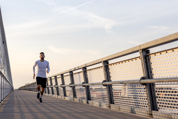 Young man in white shirt jogging on the bridge at the end of day