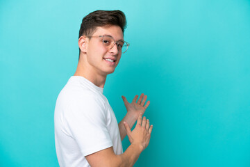 Young handsome Brazilian man isolated on blue background With glasses and presenting something