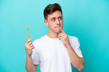 Young Brazilian man brushing teeth isolated on blue background having doubts and thinking