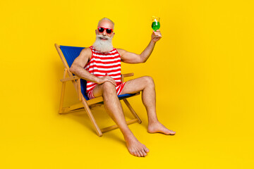 Full size photo of excited handsome man chilling lounger raise alcohol cocktail glass isolated on yellow color background