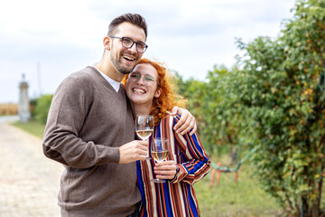 Young couple with glass of vine in hands hug and smile in vineyard
