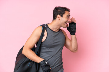 Young sport caucasian man with sport bag isolated on pink background shouting with mouth wide open...
