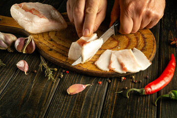 A man hands cut pork lard with a knife on a wooden cutting board. The concept of delicious peasant...