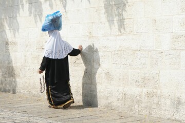 Closeup of a Islamic woman carrying a bag on her head walking by a wall