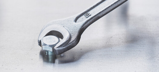 Wrench tightens bolt in steel billet. Spanner, bolt, screw and nuts.