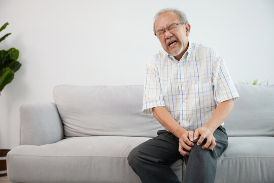 senior man suffering from knee ache on sofa