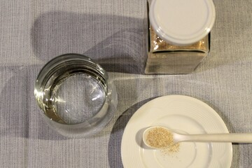 Ein Vorratsglas mit indischen Flohsamenschalen, ein Glas Wasser, ein Teelöffel zum Mitnehmen....