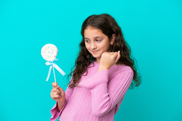 Little caucasian girl holding a lollipop isolated on blue background celebrating a victory