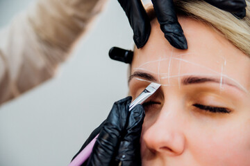The makeup artist performs long-term eyebrow styling and paints the eyebrows. Lamination of eyebrows. Professional makeup and facial care. Makes markings for permanent makeup. - obrazy, fototapety, plakaty