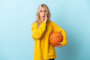 Young Russian woman playing basketball isolated on blue background whispering something with...