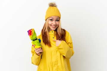 Teenager blonde girl wearing a rainproof coat over isolated white background with surprise facial expression