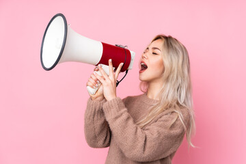 Teenager blonde girl wearing a sweater over isolated pink background shouting through a megaphone