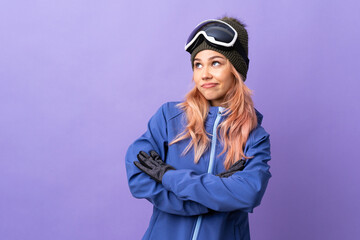 Skier teenager girl with snowboarding glasses over isolated purple background making doubts gesture while lifting the shoulders