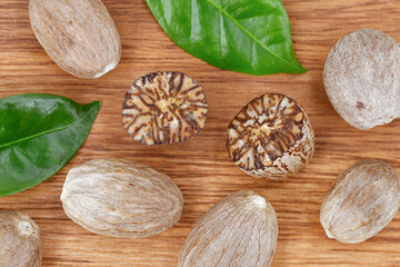 Top view of halved and whole nutmegs on a wooden background with green leaves