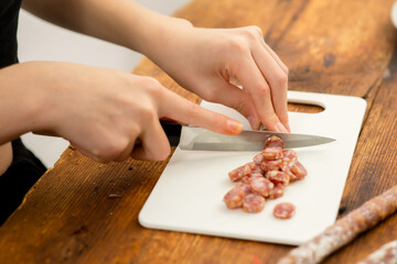 Obraz na płótnie Canvas Gastronomic precision: A woman's hands demonstrate precision in slicing sausage on a cutting board, illustrating attention to detail in culinary craftsmanship