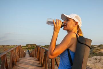 A sports girl stands drinking water from a bottle after a morning workout. 