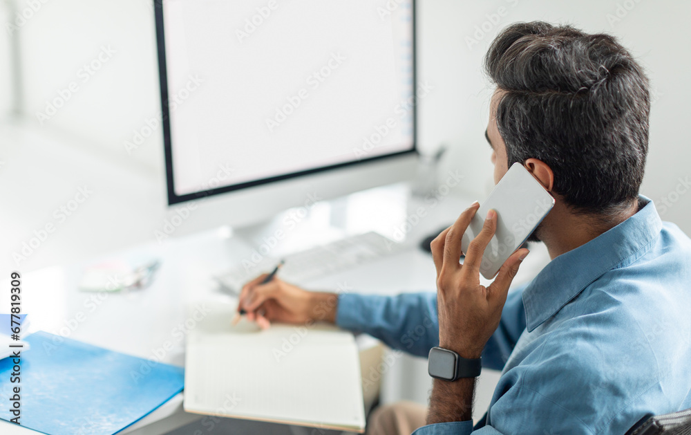 Poster businessman multitasking with phone and notes, looking at blank monitor