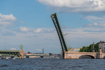Side view from tour boat of open Troitsky bascule bridge above Neva river in a sunny day with some clouds. European cityscape. Soft focus. City transportation architecture theme.
