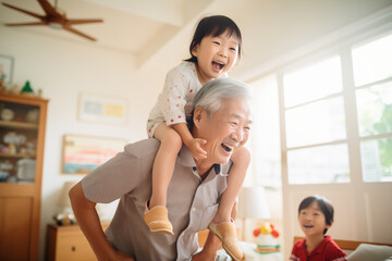 An energetic Asian grandfather carries one of his granddaughters on his shoulders, sharing enjoyable moments together indoors. The active elderly man enjoys his grandchildren.   active aging concept