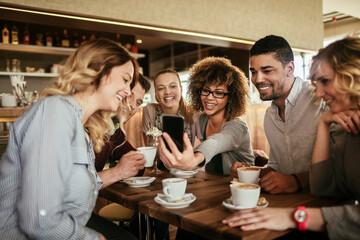 Group of Happy friends looking at smartphone in cafe together