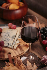 Glass of red wine served with blue cheese on dark wooden background. Autumn picnic with wine and cheese platter, fruits and dry leaves in rustic style
