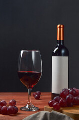 Elegant photo of a red wine bottle with a glass and grapes on the side, with a blank label to place...