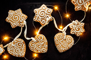 Christmas gingerbread cookies in the shapes of hearts and stars decorated with white icing on a black background.  Homemade, hand-decorated gingerbread cookies.